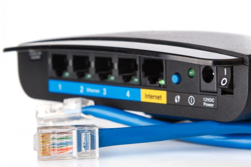 Vue rapprochée de l'arrière d'un routeur Wi-Fi noir montrant quatre ports Ethernet RJ45 numérotés, un port Internet jaune, le bouton d'appairage WPS, la prise d'alimentation 12V et l'interrupteur, avec des câbles réseau bleus au premier plan.