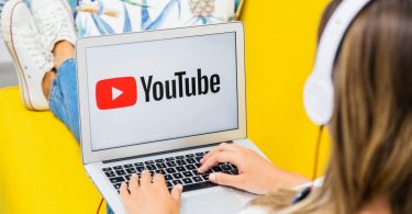 Jeune élève avec un casque audio utilisant un ordinateur portable affichant le logo YouTube, illustrant la consommation massive de vidéos et les risques d'addiction aux écrans en milieu scolaire.