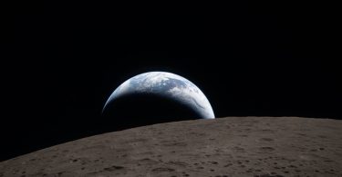 Image historique prise par l'équipage d'Artemis II depuis la capsule Orion, montrant l'éclipse solaire totale : la Lune apparaît comme un orbe noir texturé de cratères sur la face visible, masquant le Soleil dont seule la couronne lumineuse (le halo solaire) est visible dans l'espace profond. Des étoiles sont discernables en arrière-plan.