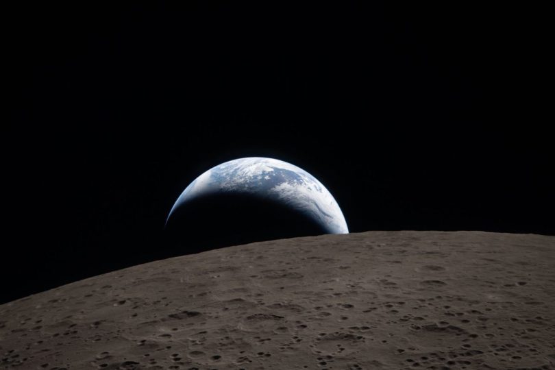 Image historique prise par l'équipage d'Artemis II depuis la capsule Orion, montrant l'éclipse solaire totale : la Lune apparaît comme un orbe noir texturé de cratères sur la face visible, masquant le Soleil dont seule la couronne lumineuse (le halo solaire) est visible dans l'espace profond. Des étoiles sont discernables en arrière-plan.