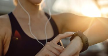 Femme en tenue de sport utilisant une montre connectée Garmin pour consulter ses données de santé lors d'une séance de fitness en extérieur au coucher du soleil.