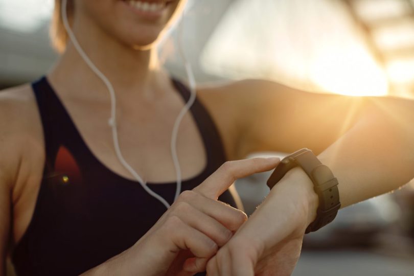 Femme en tenue de sport utilisant une montre connectée Garmin pour consulter ses données de santé lors d'une séance de fitness en extérieur au coucher du soleil.