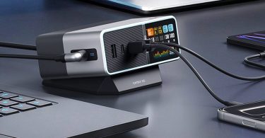 Station de charge Cuktech 30 Ultra 300W posée sur un bureau noir entre un ordinateur portable et un smartphone, avec écran LCD couleur en face avant affichant la consommation en temps réel de chaque port USB-C et USB-A en cours d'utilisation