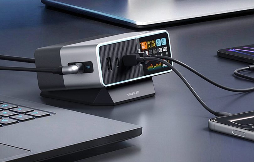 Station de charge Cuktech 30 Ultra 300W posée sur un bureau noir entre un ordinateur portable et un smartphone, avec écran LCD couleur en face avant affichant la consommation en temps réel de chaque port USB-C et USB-A en cours d'utilisation