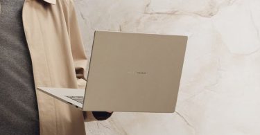 Homme portant un élégant ordinateur portable ASUS Zenbook 16 pouces beige d'une main, avec un fond de marbre de couleur similaire.