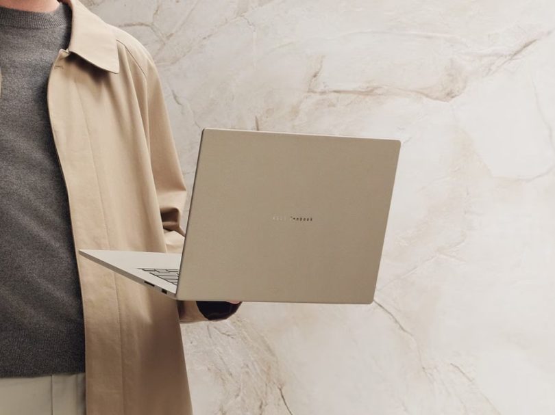 Homme portant un élégant ordinateur portable ASUS Zenbook 16 pouces beige d'une main, avec un fond de marbre de couleur similaire.