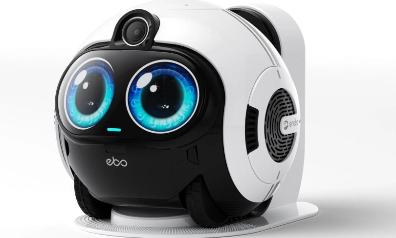 Robot compagnon EBO Max de Enabot avec ses grands yeux bleus numériques expressifs, caméra 4K intégrée et station de recharge blanche en arrière-plan.