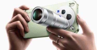 Gros plan sur un concept de Vivo X500 Pro Max vert pastel, tenu en main par un utilisateur avec une bague, arborant un module photo hybride unique : deux objectifs principaux avec logo ZEISS bleus et un objectif amovible/télescopique argenté proéminent.