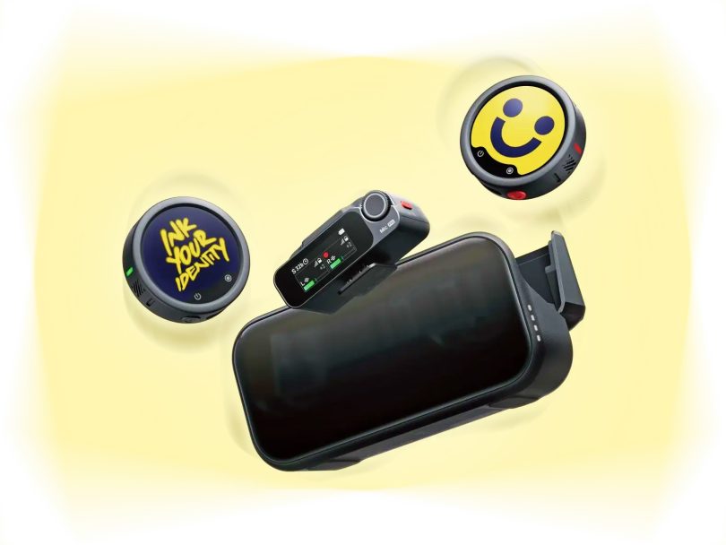 Ensemble audio Insta360 Mic Pro comprenant un récepteur avec écran E-Ink affichant les niveaux, deux émetteurs circulaires (un avec logo "INK YOUR IDENTITY", l'autre avec smiley jaune), et un boîtier de charge ouvert, sur fond jaune pastel.