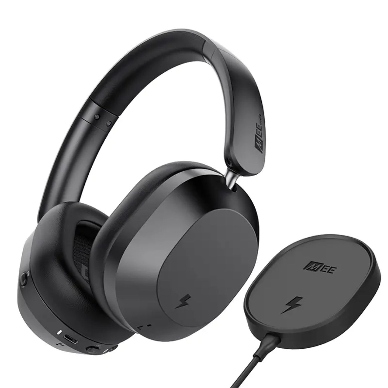 Casque sans fil over-ear MEE Audio Matrix Cinema 3D 2026 noir mat avec coussinets memory foam ultra-doux noirs, photo officielle 3/4 montrant l'arceau réglable avec logo MEE audio gravé, le port USB-C de charge filaire, l'entrée jack 3,5 mm pour mode wired, le bouton physique CinemaEAR, et le pad de charge sans fil magnétique circulaire MEE inclus avec son câble USB-C, ensemble destiné à la consommation TV et cinéma avec spatial audio à head tracking en temps réel