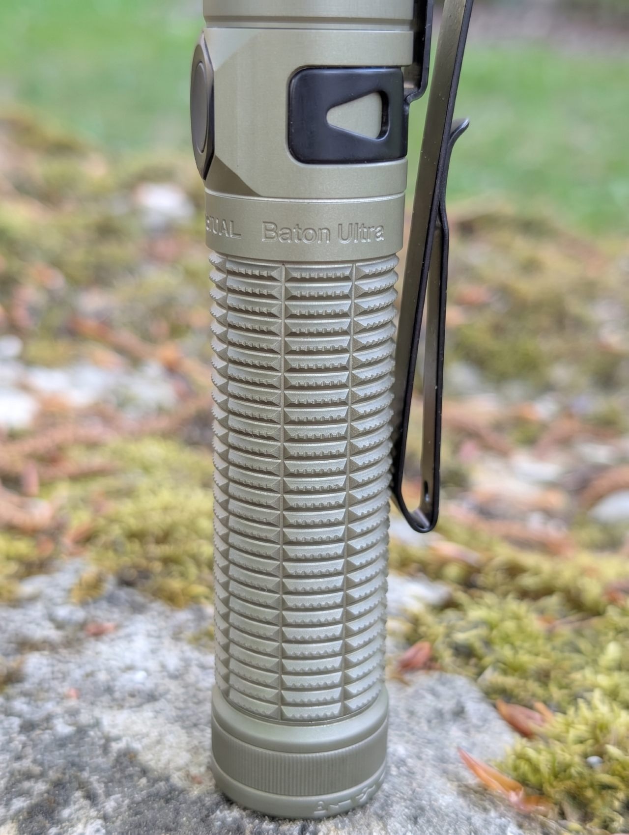 Olight Baton Ultra Desert Tan - vue de profil, knurling en pyramides et clip bidirectionnel sur fond outdoor