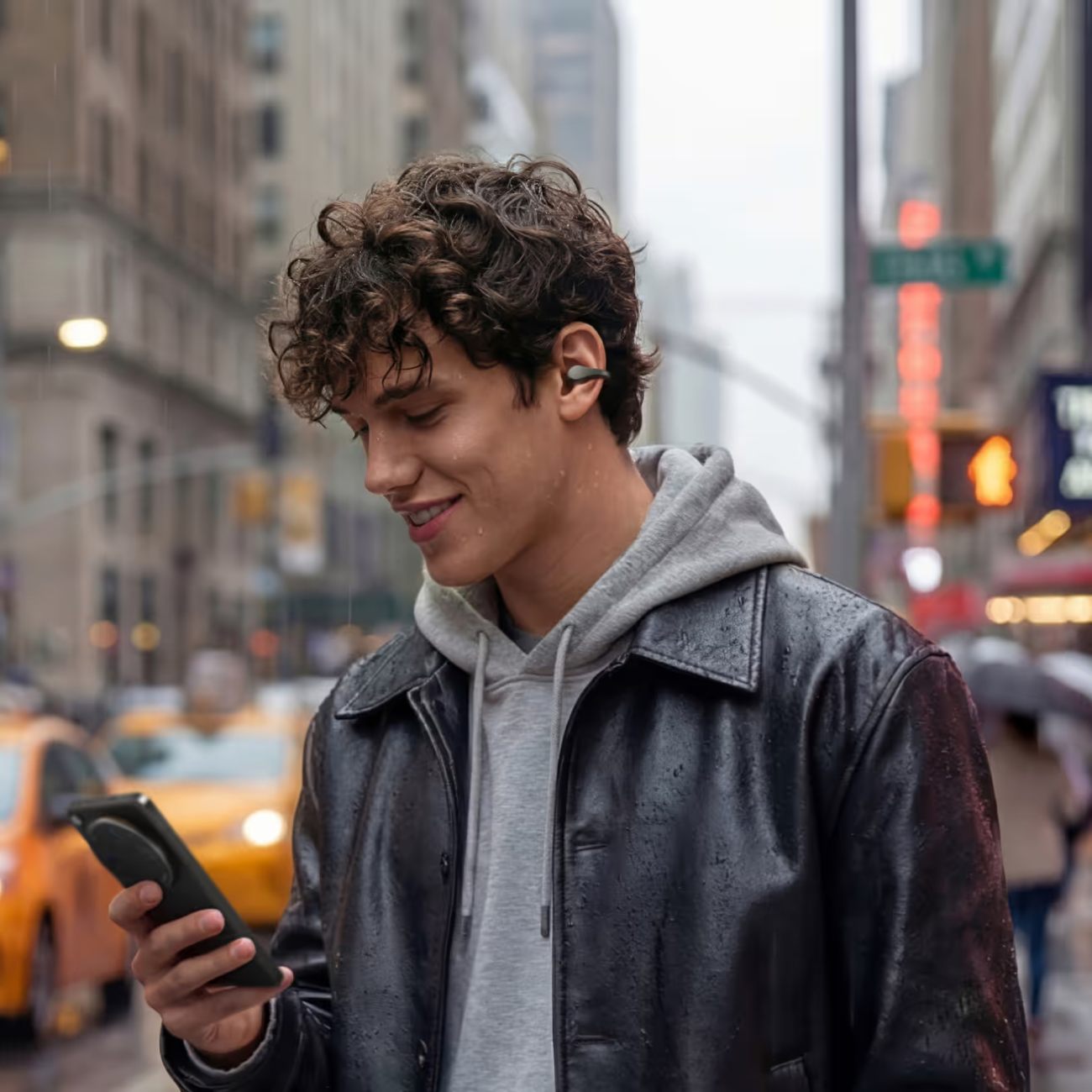 Jeune homme en ville sous une pluie légère utilisant les écouteurs OPPO Enco Clip2 (Slate Grey). Les gouttes d'eau sur son visage et sa veste soulignent la certification IP55 de résistance aux éclaboussures et à la poussière.