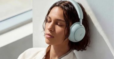 Femme aux cheveux bruns courts portant le casque Soundcore Space 2 en finition Seafoam Green vert pastel, yeux fermés, adossée à un mur clair éclairé par la lumière naturelle