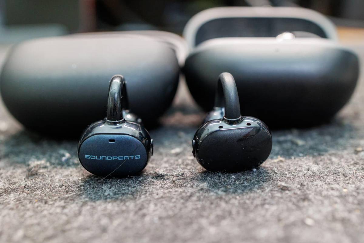 SOUNDPEATS UU2 Ear Cuff présenté en gros plan à côté d'un écouteur open-ear concurrent, avec leurs boîtiers de charge respectifs en arrière-plan