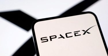 Logo SpaceX noir sur fond blanc affiché sur un écran de smartphone, avec un "X" stylisé en arrière-plan flou, illustrant l'annonce de l'option d'achat de Cursor par Elon Musk.