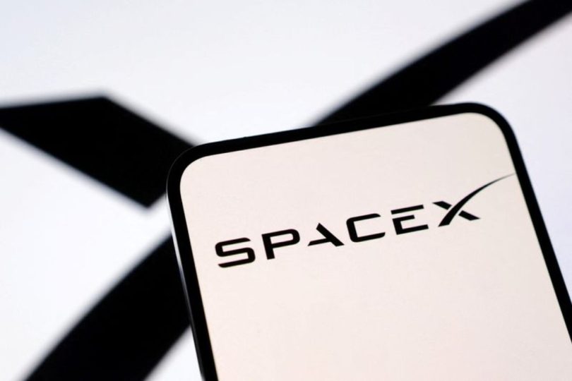 Logo SpaceX noir sur fond blanc affiché sur un écran de smartphone, avec un "X" stylisé en arrière-plan flou, illustrant l'annonce de l'option d'achat de Cursor par Elon Musk.