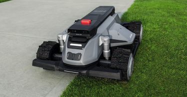 Tondeuse robot TerraMow-X AWD grise au design futuriste avec roues motrices tout-terrain, tondant avec précision la bordure d'une pelouse longeant une allée en béton.