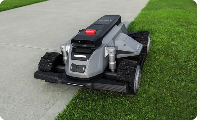 Tondeuse robot TerraMow-X AWD grise au design futuriste avec roues motrices tout-terrain, tondant avec précision la bordure d'une pelouse longeant une allée en béton.