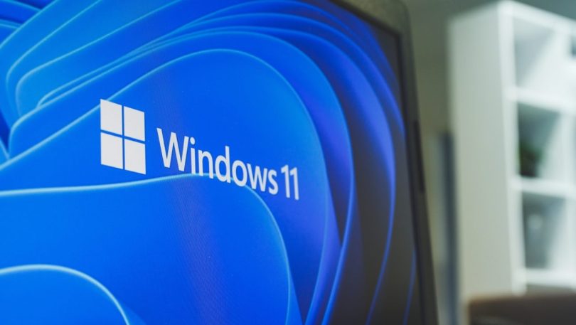 Description : Gros plan sur l'écran d'un ordinateur portable affichant le logo officiel et le texte "Windows 11" sur un fond bleu abstrait et moderne.