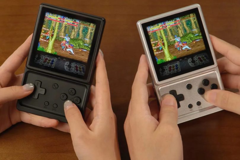 Deux consoles portables Anbernic RG Rotate, l'une en plastique ABS noir et l'autre en aluminium argenté, affichant un jeu de combat rétro sur leur écran LCD carré de 3,5 pouces. On distingue le D-pad et les boutons d'action sous l'écran pivotant.