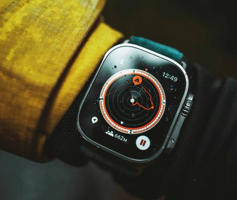 Gros plan sur le cadran de l'Apple Watch Ultra 4 en conditions réelles affichant une interface de navigation plein air. Des gouttes d'eau sur l'écran et le boîtier robuste illustrent sa résistance, s'appuyant sur ses nouveaux capteurs de santé et de sport.