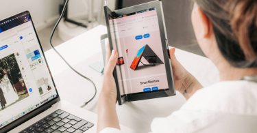 Utilisateur tenant en main l'écran portable AMOLED pliable Single Flex Pro d'Aura Displays de 13,3 pouces, connecté via USB-C à un ordinateur portable sur un espace de travail.