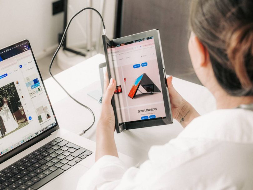 Utilisateur tenant en main l'écran portable AMOLED pliable Single Flex Pro d'Aura Displays de 13,3 pouces, connecté via USB-C à un ordinateur portable sur un espace de travail.