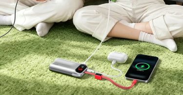 Batterie externe Ugreen PB610 45W argentée au design incurvé, dotée d'un écran affichant un emoji, posée sur un tapis vert et chargeant simultanément un iPhone et des écouteurs via son câble rouge tressé intégré.