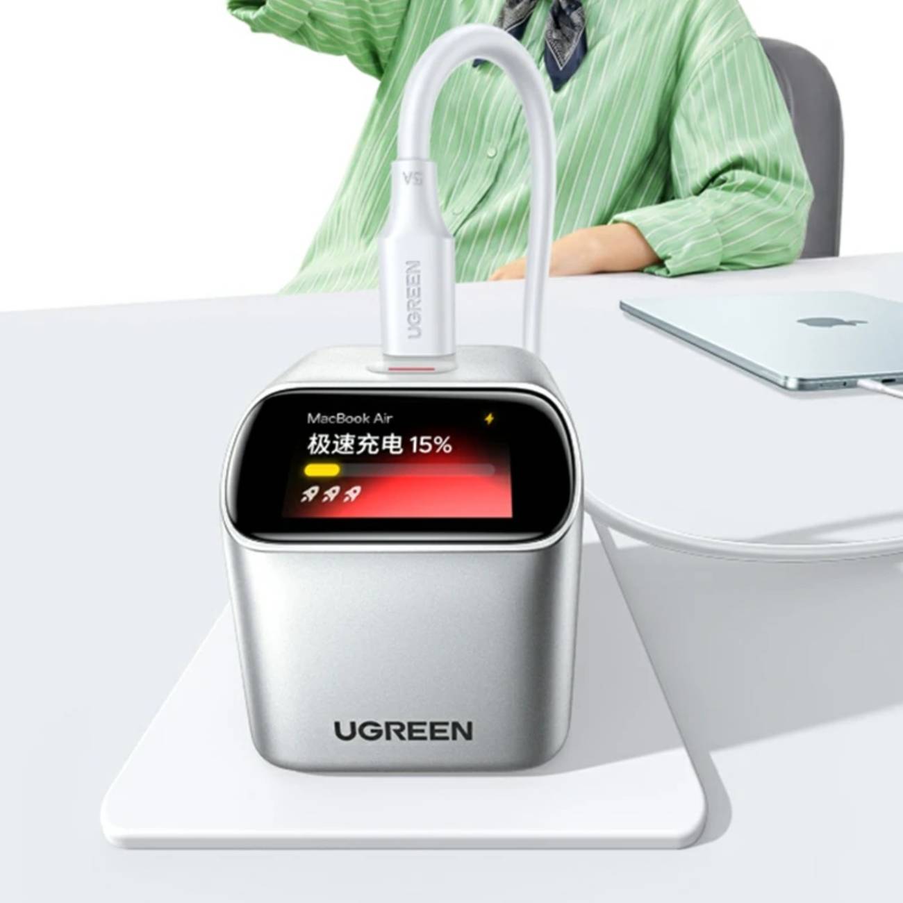 Chargeur Ugreen X740 45W argenté posé sur un bureau blanc et connecté via un câble USB-C. L'écran numérique affiche la mention "MacBook Air" ainsi que le niveau de batterie "15%" avec une barre de progression, démontrant la reconnaissance de l'appareil en cours de charge.
