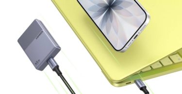 Chargeur ultra-compact Ugreen Nexode Air 45W gris au format "biscuit", connecté par un câble USB-C tressé à un ordinateur portable jaune sur lequel repose un smartphone.