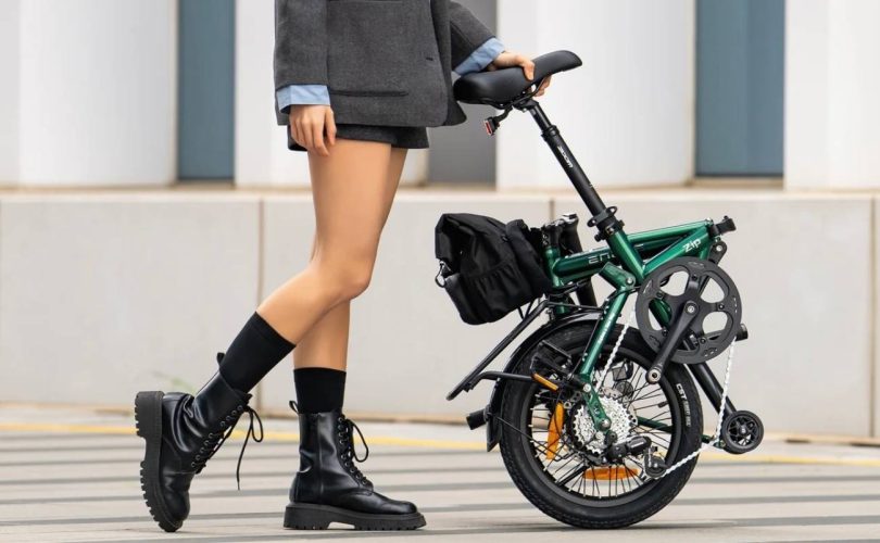 Personne marchant en ville en tenant par la selle le vélo électrique pliable Engwe Zip vert olive, illustrant son format ultra-compact de 62,5 cm une fois replié sur lui-même.