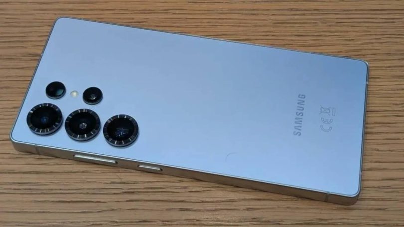 Dos d'un smartphone Samsung Galaxy S26 bleu clair avec ses capteurs photo texturés, posé sur une table en bois, illustrant le modèle premium touché par la hausse des prix.