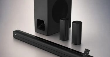 Système home cinéma iBall Cinebar 560 complet, barre de son noire trois voies, caisson de basses cubique, deux satellites cylindriques sans-fil et télécommande, posés sur fond gris dégradé.