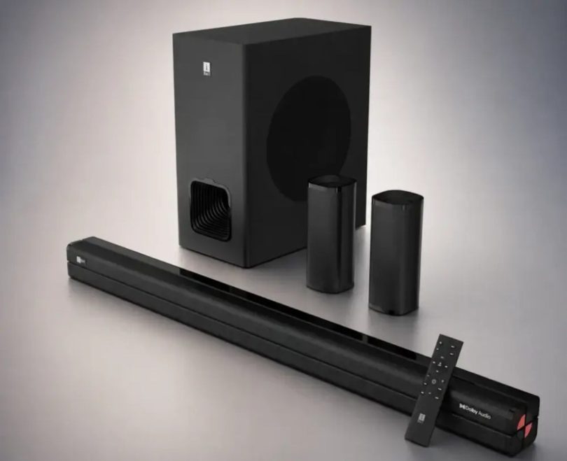 Système home cinéma iBall Cinebar 560 complet, barre de son noire trois voies, caisson de basses cubique, deux satellites cylindriques sans-fil et télécommande, posés sur fond gris dégradé.