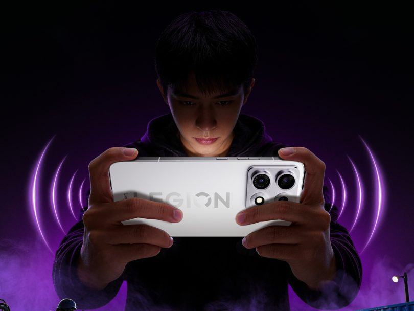 Smartphone gaming Lenovo Legion Y70 2026 coloris blanc tenu en mode paysage par un joueur, ambiance violette néon avec ondes sonores stylisées et bloc photo arrière imposant