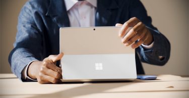 Personne ajustant le support intégré d'une tablette Microsoft Surface Pro 12 argentée, avec le logo Windows visible au dos, sur un bureau.
