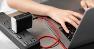 Power bank Solly 300W noire branchée directement sur une multiprise grâce à sa fiche secteur intégrée, rechargeant un ordinateur portable via un câble USB-C rouge tressé.