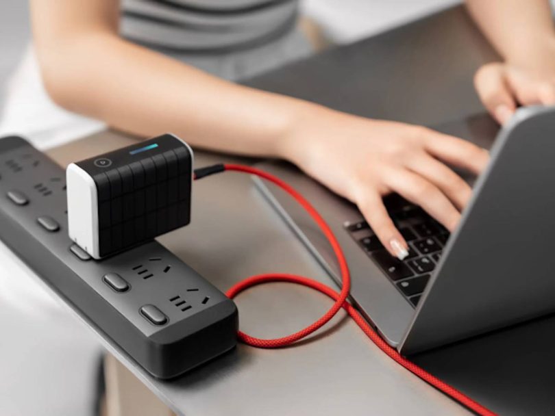 Power bank Solly 300W noire branchée directement sur une multiprise grâce à sa fiche secteur intégrée, rechargeant un ordinateur portable via un câble USB-C rouge tressé.
