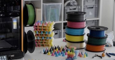Imprimante 3D sur un plan de travail entourée de bobines de filaments CMYKW et de dizaines de petits cônes de test illustrant les nuances obtenues par la technologie de mélange ColorMix.