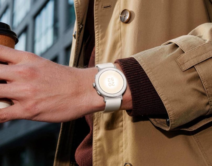 Realme Watch S5 coloris Sand White portée au poignet, boîtier rond au profil plat, trois boutons latéraux et écran AMOLED circulaire affichant l'heure en extérieur.
