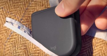Souris pliante Logitech repliée totalement à plat glissée dans la poche poitrine d'une veste en tweed marron, démonstration du gain d'encombrement pour la mobilité professionnelle