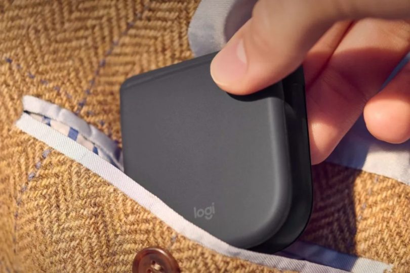 Souris pliante Logitech repliée totalement à plat glissée dans la poche poitrine d'une veste en tweed marron, démonstration du gain d'encombrement pour la mobilité professionnelle
