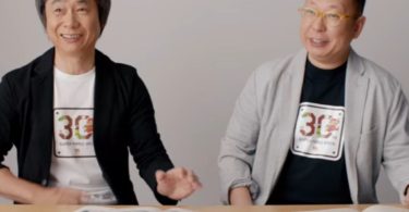 Takashi Tezuka et Shigeru Miyamoto, deux légendes de Nintendo, posent côte à côte avec un t-shirt commémoratif des 30 ans de Super Mario Bros, devant des documents de game design étalés sur une table.
