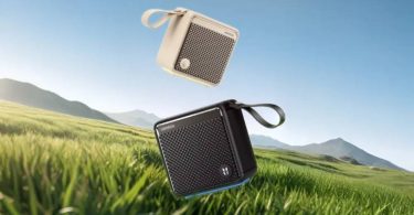 Enceinte Bluetooth Ugreen M3 en version noire et beige, avec dragonne et grille acoustique, en lévitation au-dessus d'un paysage de prairie et de montagnes, illustrant son usage outdoor et sa certification IP66.