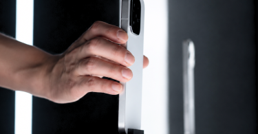 Main saisissant le profil d'un smartphone haut de gamme argenté sur un présentoir lumineux, illustrant le design premium du futur Xiaomi 17 Max.