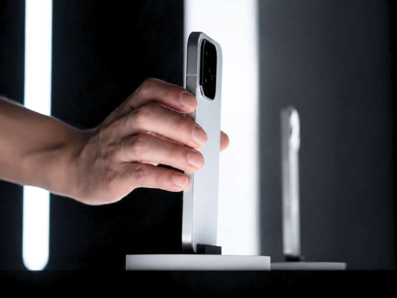 Main saisissant le profil d'un smartphone haut de gamme argenté sur un présentoir lumineux, illustrant le design premium du futur Xiaomi 17 Max.