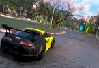 Capture d'écran du jeu Forza Horizon 6 montrant une Toyota Supra noire et jaune négociant un virage sur un circuit asphalté, entouré de cerisiers en fleurs (sakura) typiques des paysages japonais.