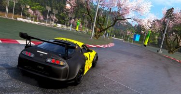 Capture d'écran du jeu Forza Horizon 6 montrant une Toyota Supra noire et jaune négociant un virage sur un circuit asphalté, entouré de cerisiers en fleurs (sakura) typiques des paysages japonais.
