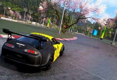 Capture d'écran du jeu Forza Horizon 6 montrant une Toyota Supra noire et jaune négociant un virage sur un circuit asphalté, entouré de cerisiers en fleurs (sakura) typiques des paysages japonais.