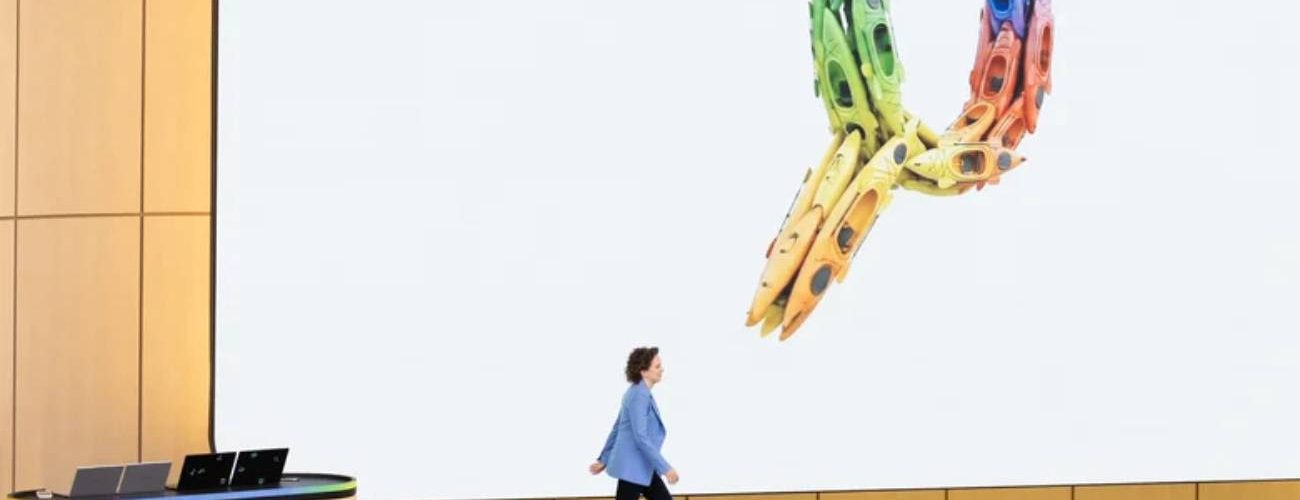Conférencière marchant sur scène devant un écran géant affichant un logo Google formé de kayaks colorés, illustrant de manière créative les engagements de l'entreprise concernant la gestion de l'eau.